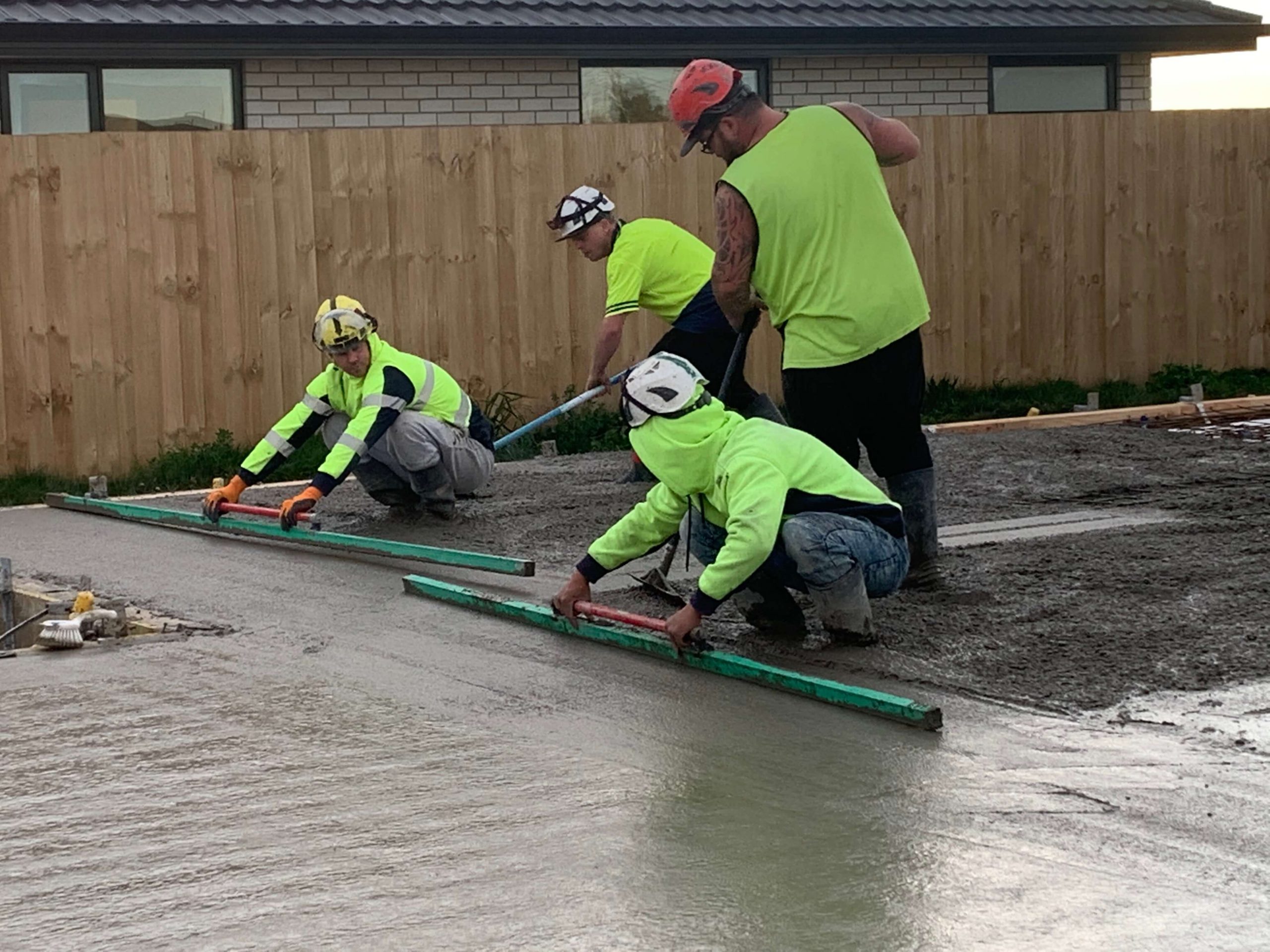 four construction males screeding a concrete foundation